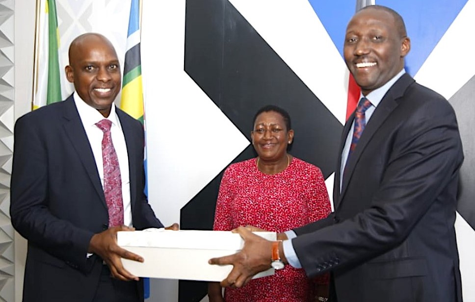 Mr. David Mugonyi (left) recieves instruments of office from his predecessor Mr. Christopher Wambua (right) when he assumed office as the Director General of the Communications Authority of Kenya today. Looking on is Ms. Mary Mungai, the CA Board Chairperson.